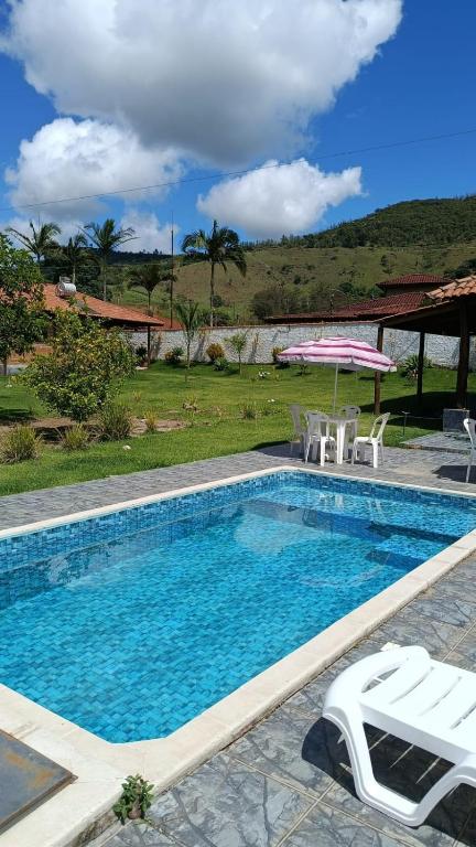 uma grande piscina com cadeiras e um guarda-sol em Chacara Sossego em Monte Sião