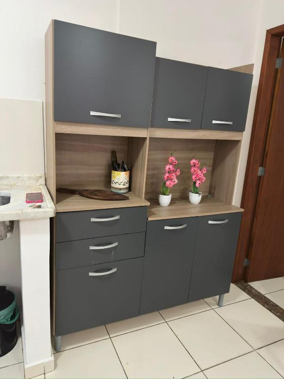 a kitchen with grey cabinets and pink flowers on a shelf at Departamento portal de ferradura in Búzios