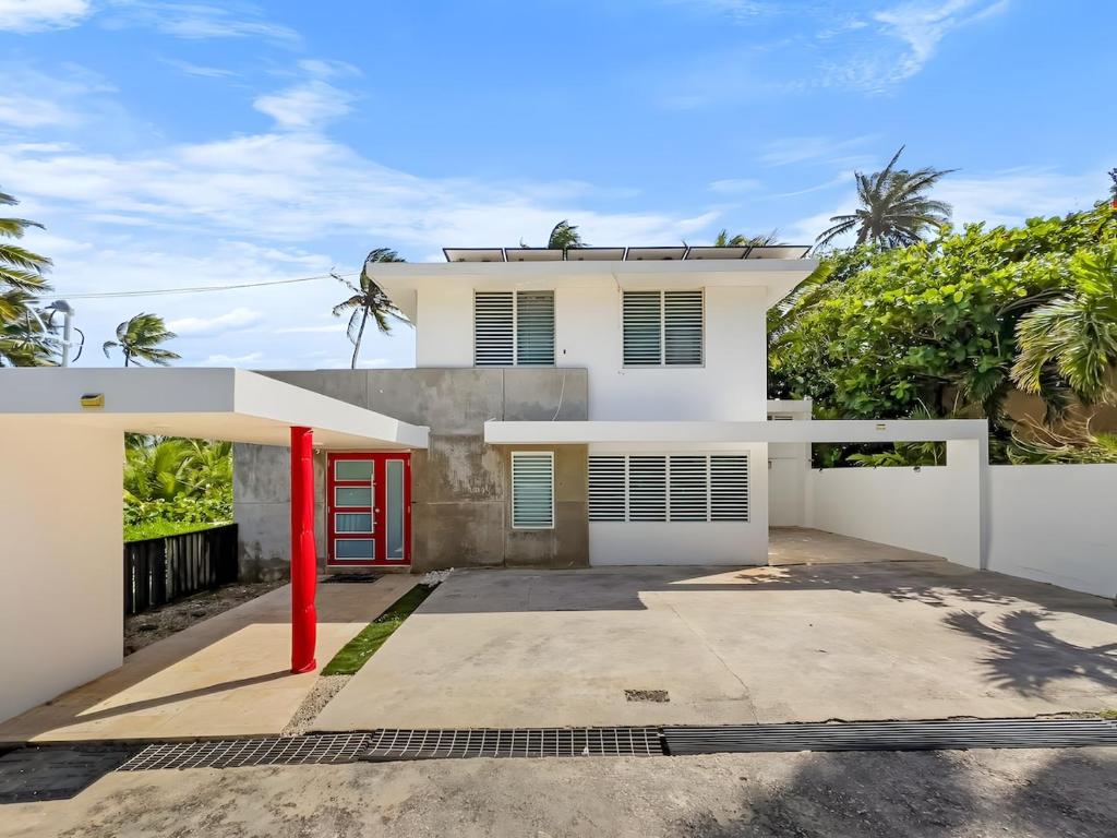 una casa blanca con una puerta roja en Villa Capitán Modern Stay Near Beach with pool, en Vega Alta