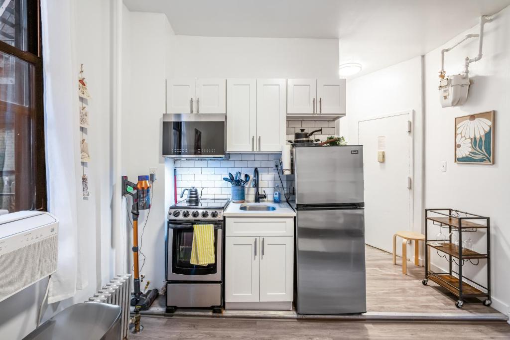 a kitchen with white cabinets and a stainless steel refrigerator at Private One Bedroom Apartment in Times Square & Central Park in New York