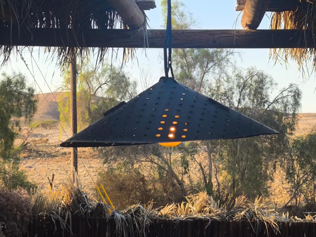 een hangende lamp die aan een gebouw hangt met een veld op de achtergrond bij הבית החום בערבה in Sappir