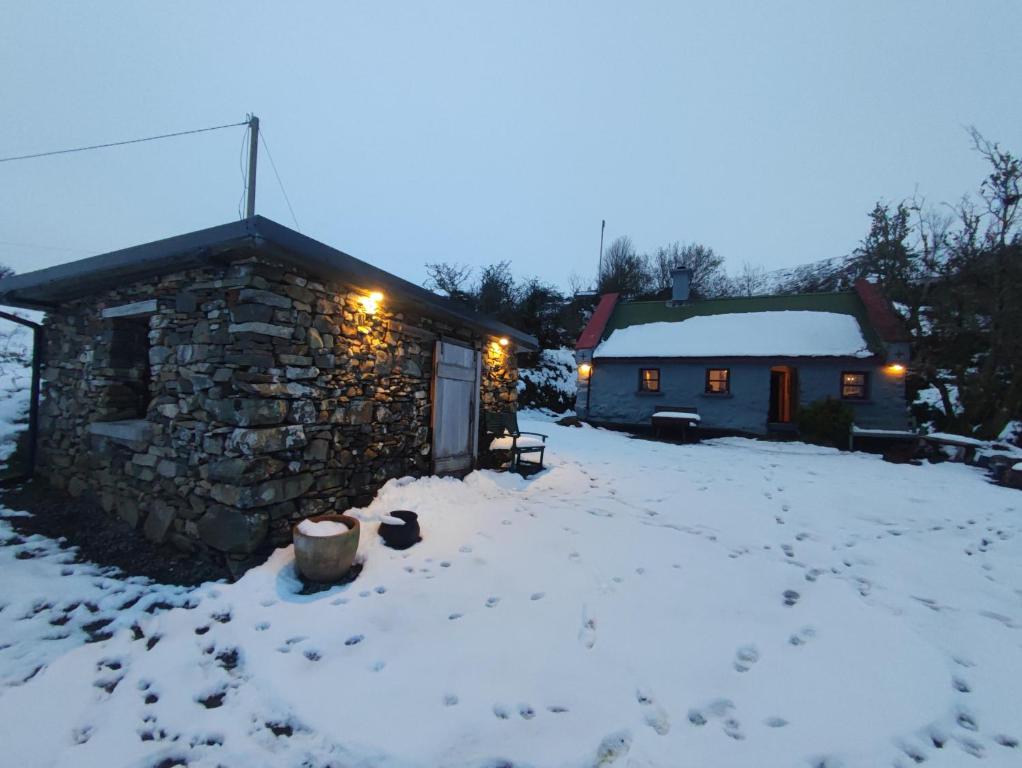 Mountain Cottage with Barn Sauna, Clonbur, Galway في Clonbur: كوخ حجري في الثلج ليلاً