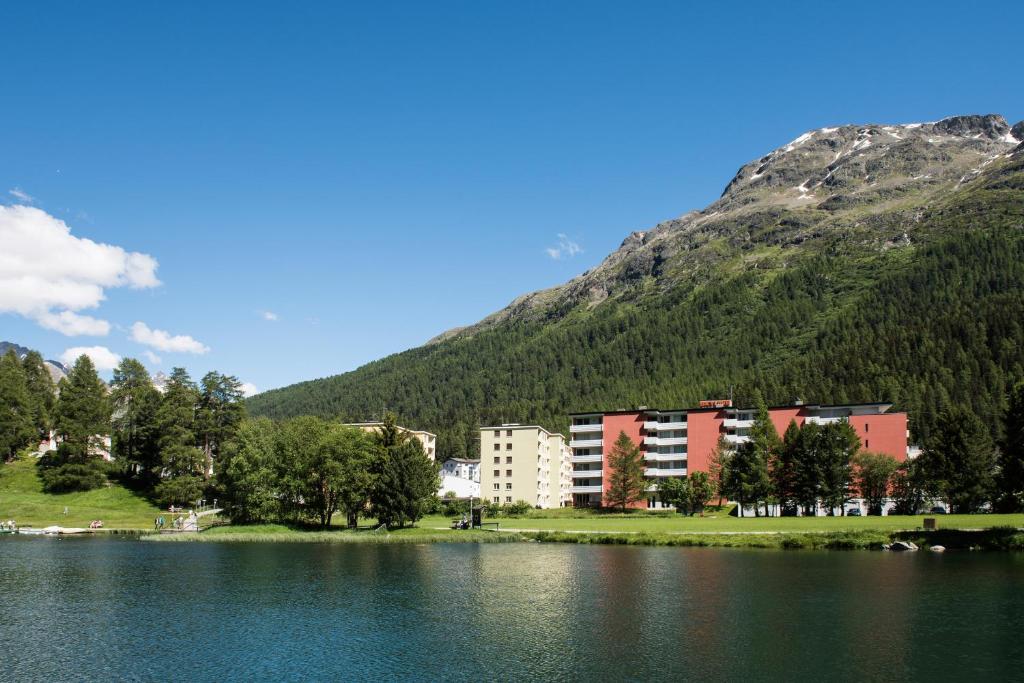 a hotel on the shore of a lake with a mountain at Skyline House Ferienapartments in St. Moritz