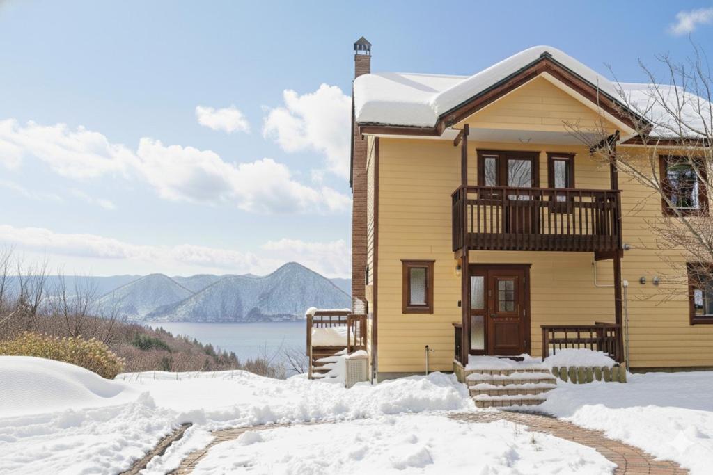 a yellow house with a balcony in the snow at Cloud9 Toya in Lake Toya