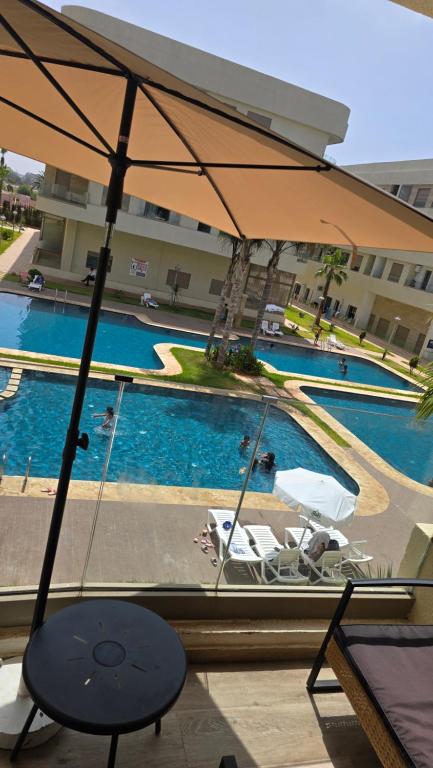 appartement résidence garden paradise plage bouznika في بوزنيقة: طاولة مع مظلة بجانب مسبح