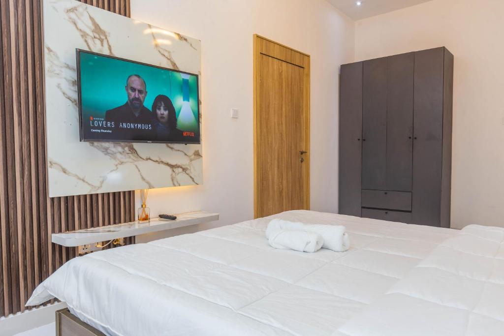 Luxury one bedroom apartment lekki phase 1 في ليكى: غرفة نوم بسرير ابيض وتلفزيون بشاشة مسطحة