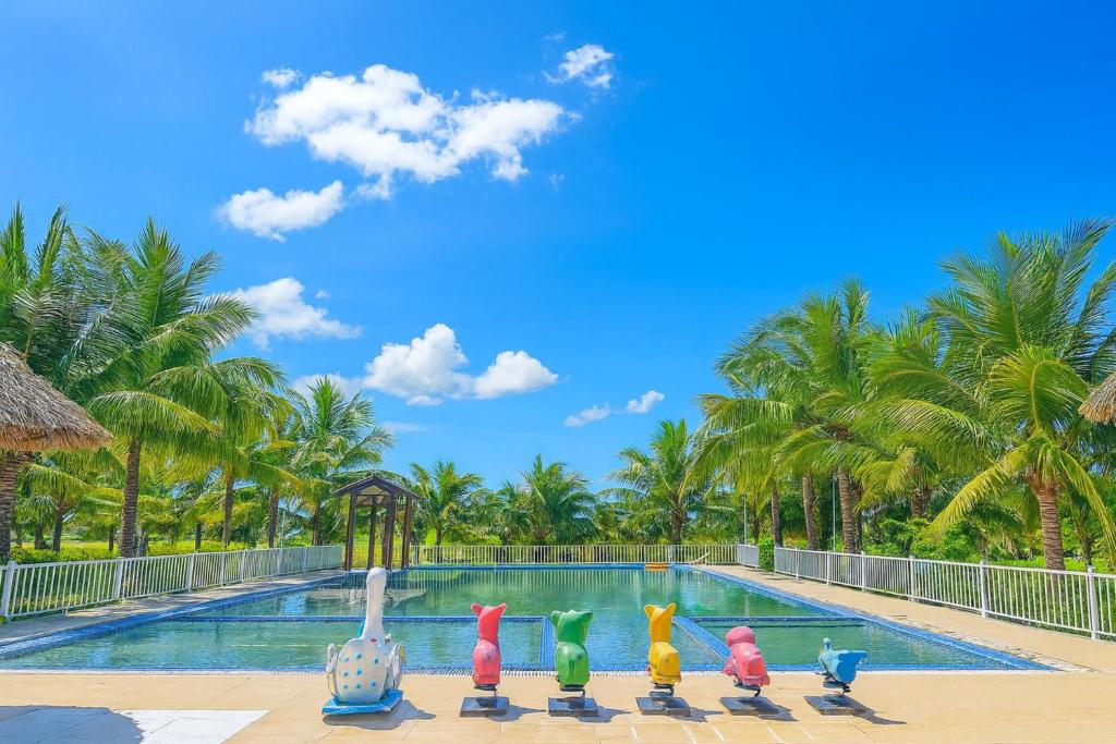 a pool at a resort with a row of colorful chicken statues at Happy Garden Hồ Tràm in Ho Tram