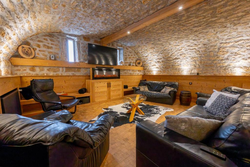 sala de estar con muebles de cuero y pared de piedra. en La Fromagerie - Gîte d'exception à La Mouille, en La Mouille
