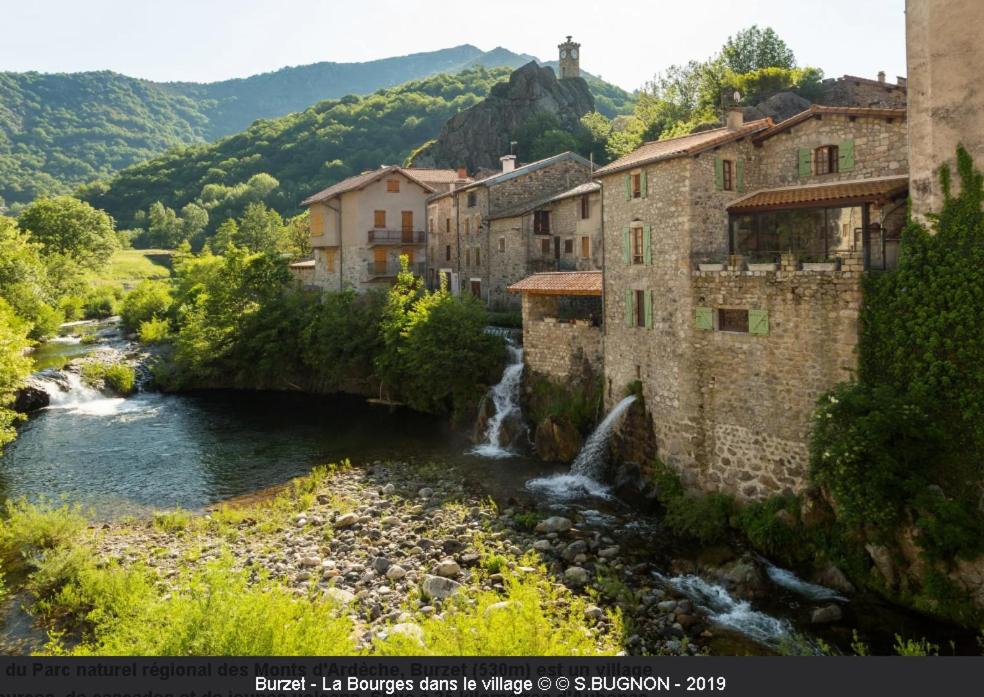 a river in a town with buildings and a waterfall at Charmant studio en Ardèche - village médiéval in Burzet