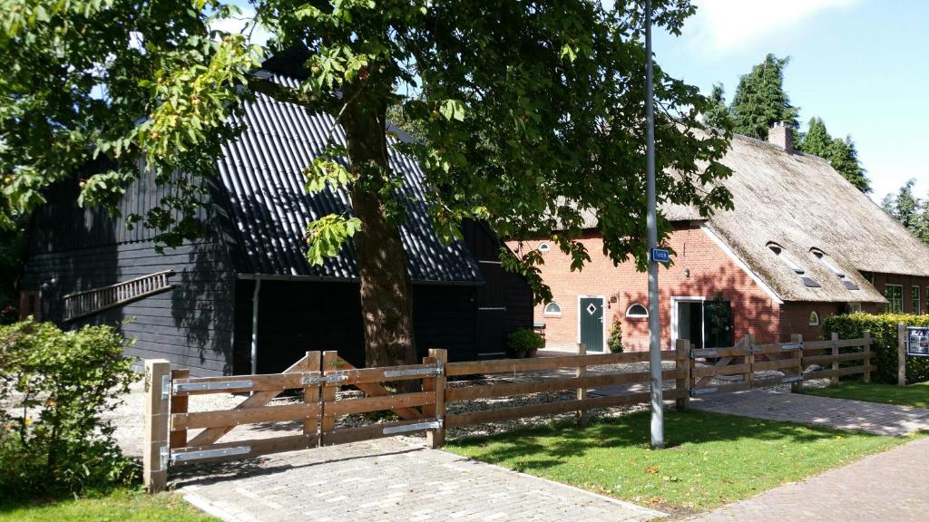 uma cerca de madeira em frente a um edifício com uma árvore em bij Saar em Zwinderen