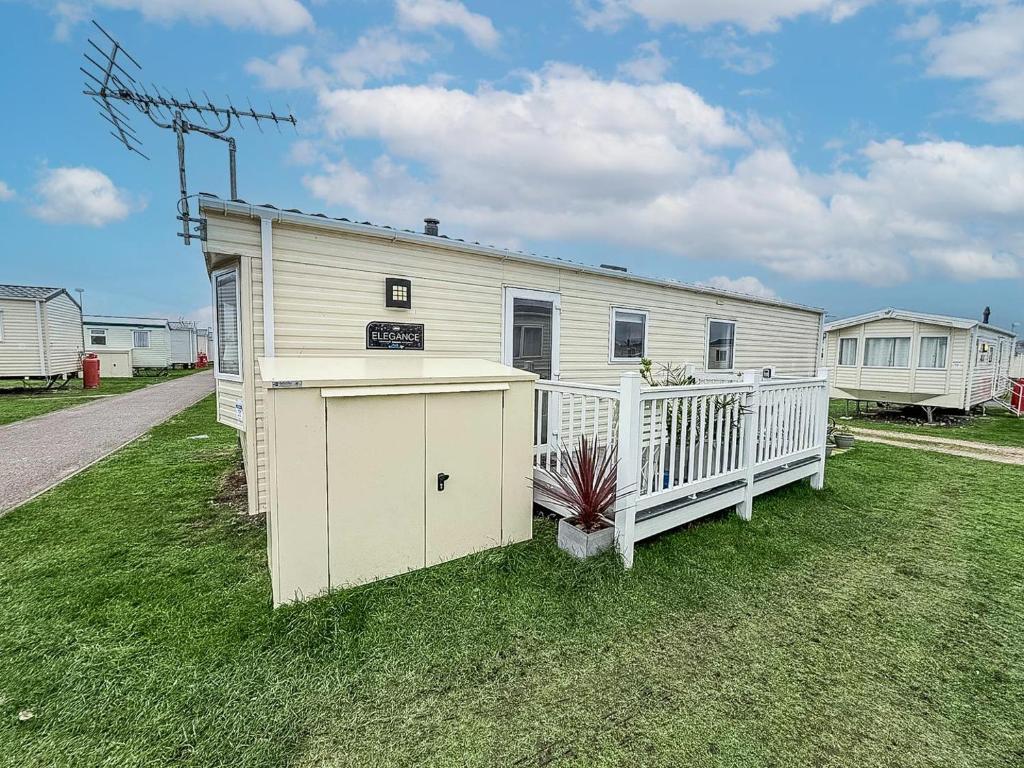 Cosy 6 Berth Caravan With Side Decking At Kessingland Beach, Suffolk Ref 90031Sv في Benacre: مبنى أبيض صغير مع شرفة على العشب