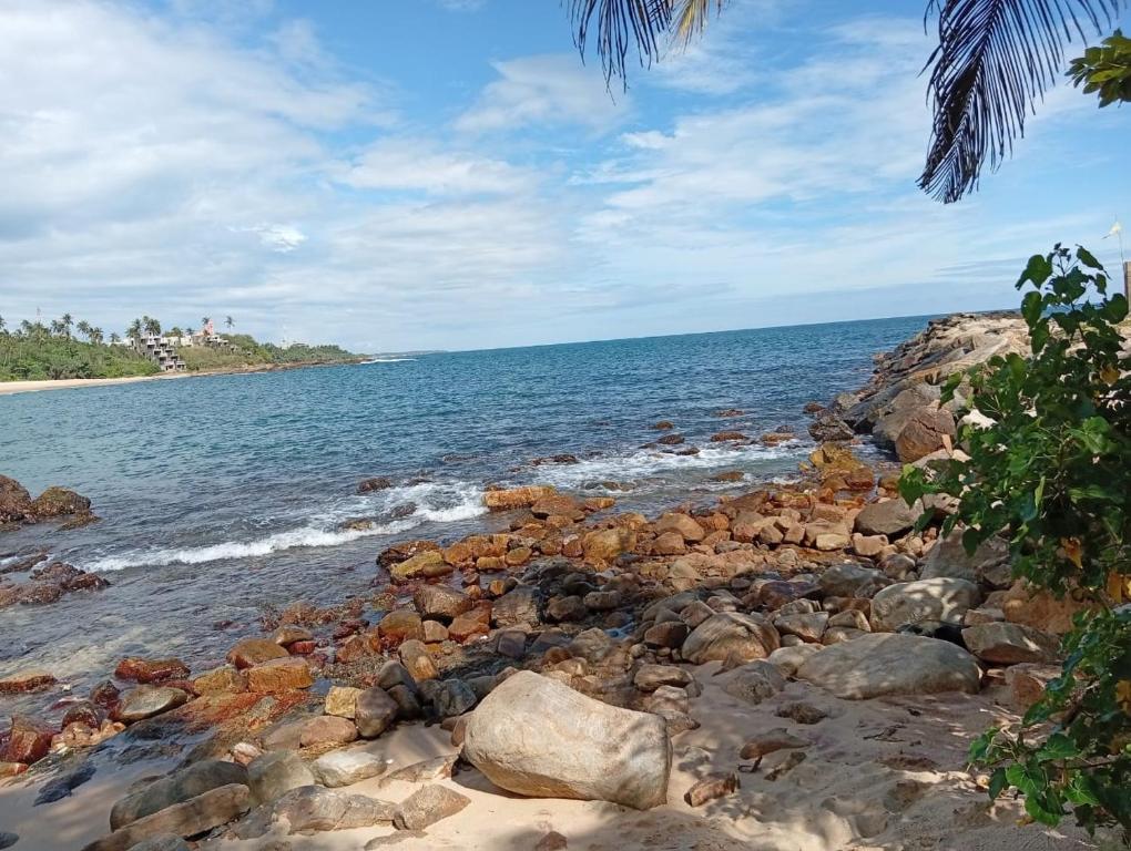 une plage avec des rochers et l'océan par temps nuageux dans l'établissement Bay Beach dom stay, à Tangalle