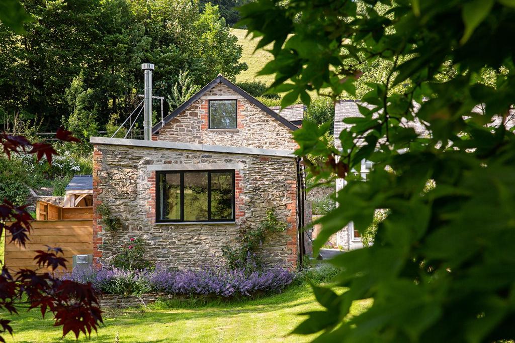 ein Steinhaus in einem Garten mit lila Blumen in der Unterkunft Coombe Farm Goodleigh - The Stables in Goodleigh