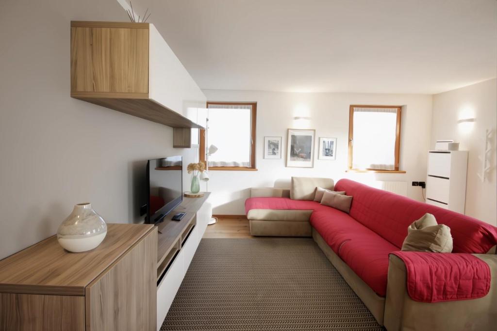 un soggiorno con un divano rosso e una TV di CASA BEBA - Cavalese Olimpiadi 2026 Dolomiti Affitti a Cavalese