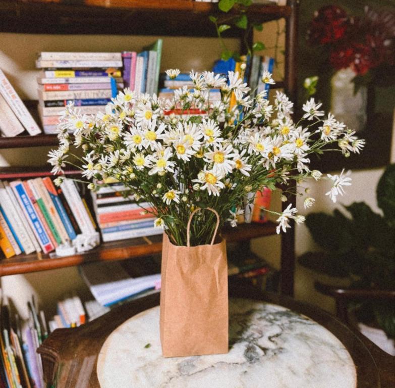 eine Vase voller weißer und gelber Blumen auf einem Tisch in der Unterkunft Tropical land little Hanoi homestay in Hanoi