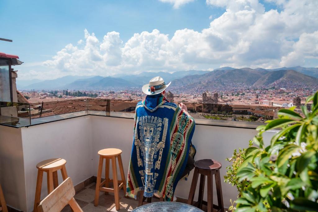 Un hombre sentado en un balcón mirando la ciudad. en Hostal Casa Del Inka, en Cusco