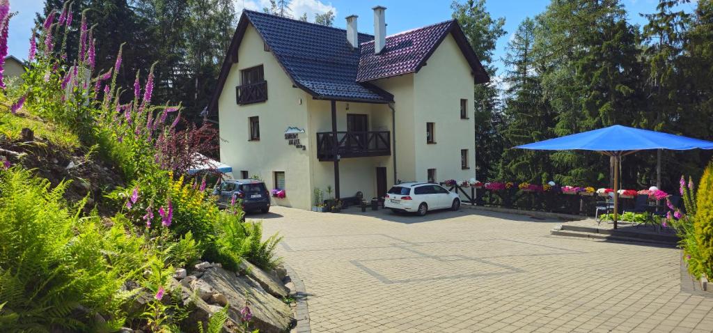 een wit huis met een blauwe paraplu naast een parkeerplaats bij Szafirowy Zakątek in Karpacz