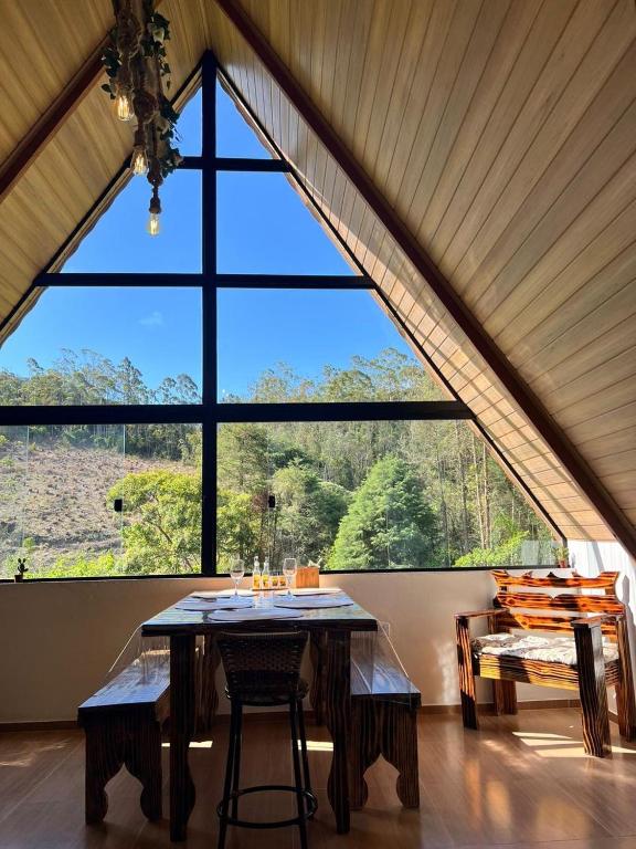 a dining room with a table and a large window at Chalé Alpes da Nascente in Salesópolis