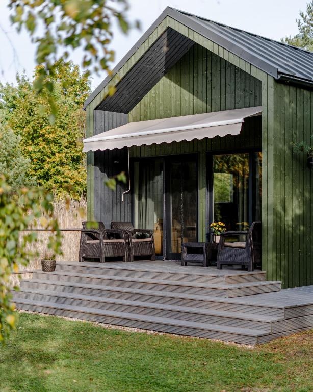 a green house with a wooden deck with chairs at Ciemzeres 2 in Engure
