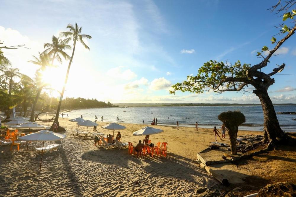 um grupo de pessoas sentadas numa praia com guarda-sóis em Casa Marea a 300 M do mar - 10 min de Serra Grande em Ilhéus
