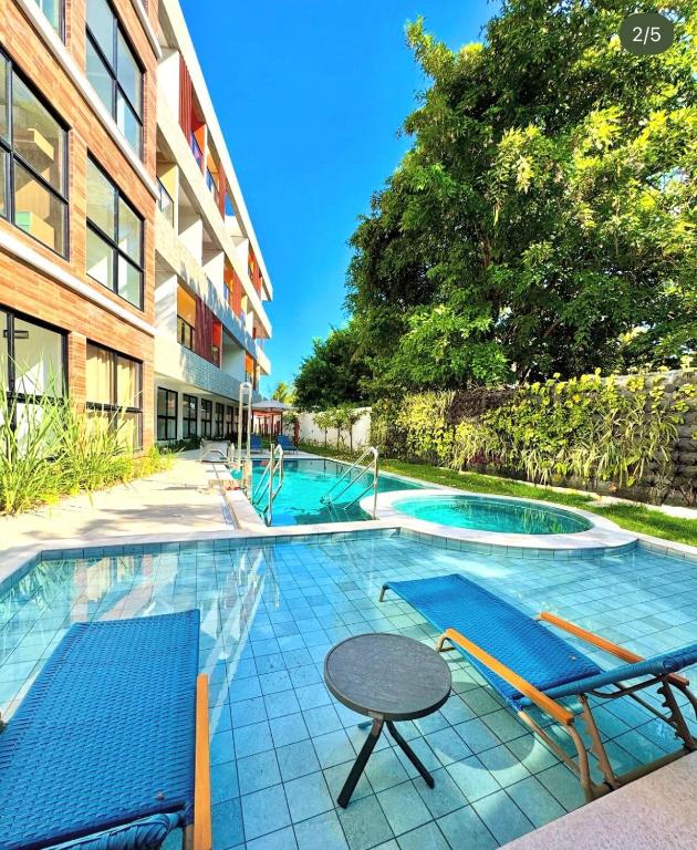 a swimming pool with chairs and a table next to a building at Maré alta flat 213 in Tamandaré