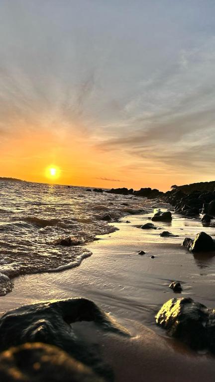a sunset over the ocean with rocks in the sand at Luz de Maria in Belém