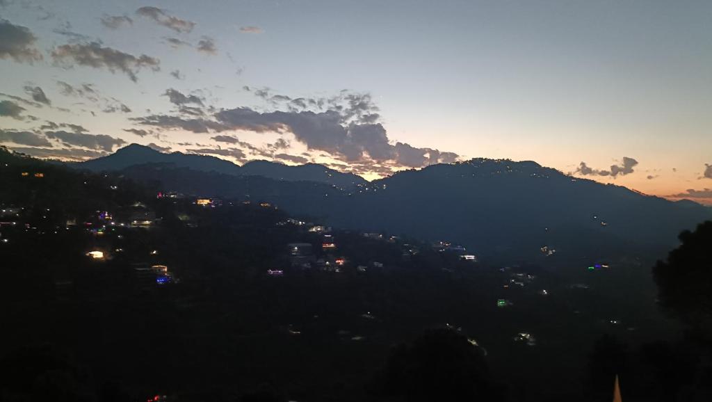 a view of a city with the sun setting behind mountains at Amazing Valley View in Kasauli