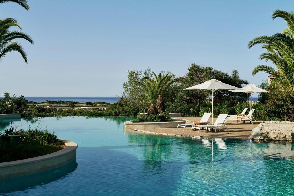 a swimming pool with chairs and umbrellas in a resort at The Westin Resort, Costa Navarino in Romanós