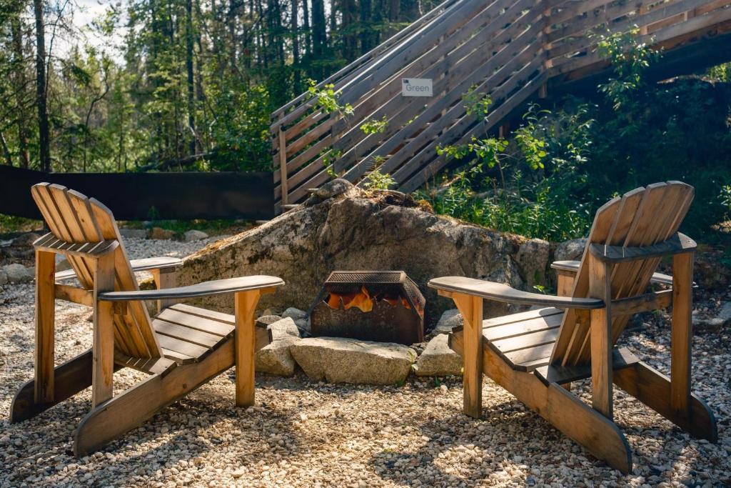 two wooden chairs sitting next to a fire pit at Black Spruce - Orange Door in Whitehorse