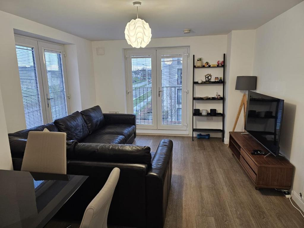 a living room with a black leather couch and a television at Stylish 2-Bed Flat with Open-Plan Living plus Parking in Edinburgh