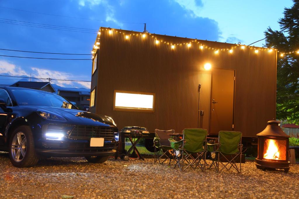 Un coche aparcado junto a unas sillas y un edificio. en Fuji Time Traveler BBQが楽しめる 河口湖湖畔すぐそば 6名宿泊可のトレーラーハウス, en Azagawa