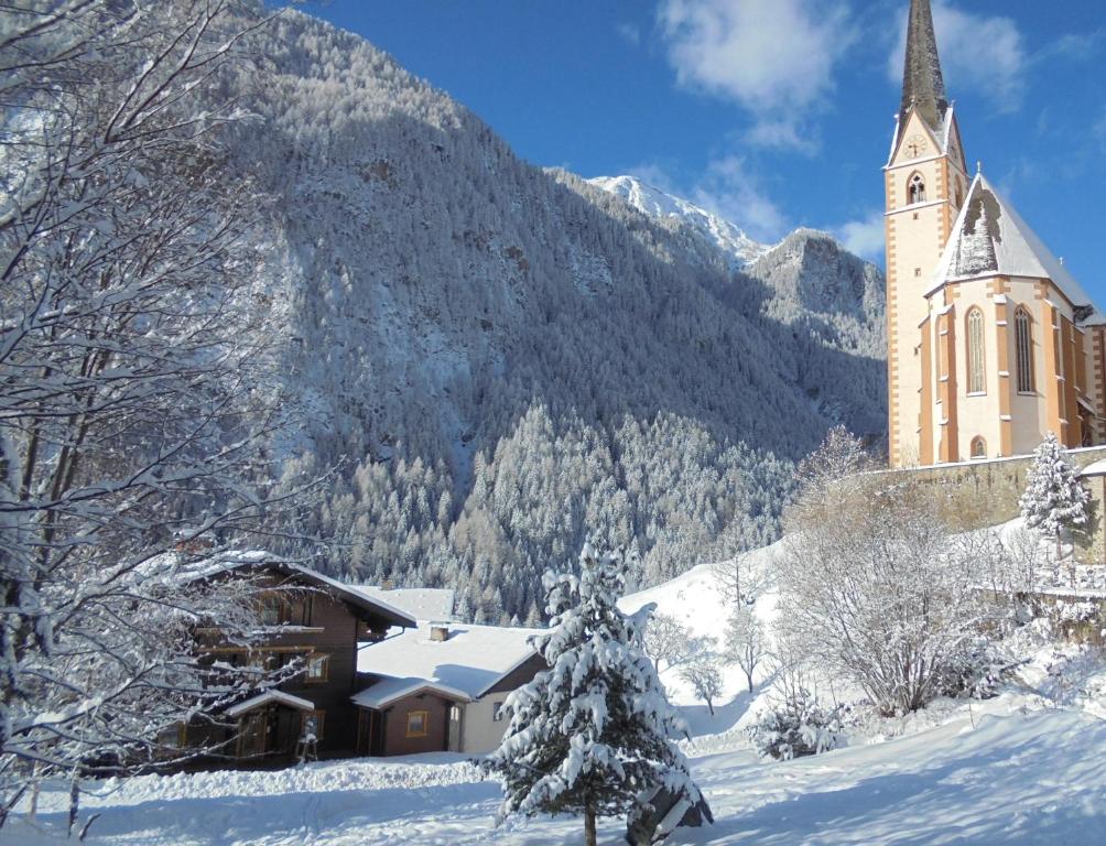una iglesia en la nieve frente a una montaña en Ferienhaus Unterkircher-Wallner, en Heiligenblut