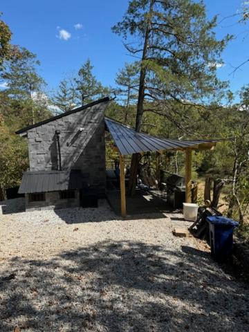 un piccolo edificio in pietra con un tetto nel bosco di Kings River Micro Cabin a Eureka Springs