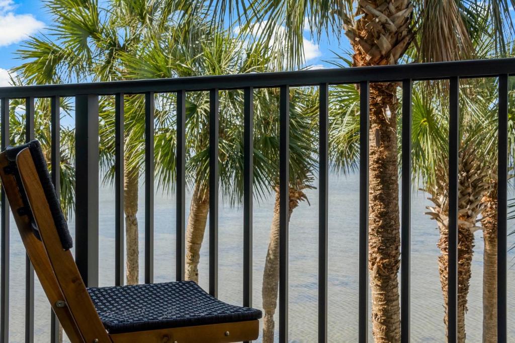Una silla en un balcón con palmeras y la playa. en Sandestin Bayfront Studio with balcony and breathtaking views, en Destin