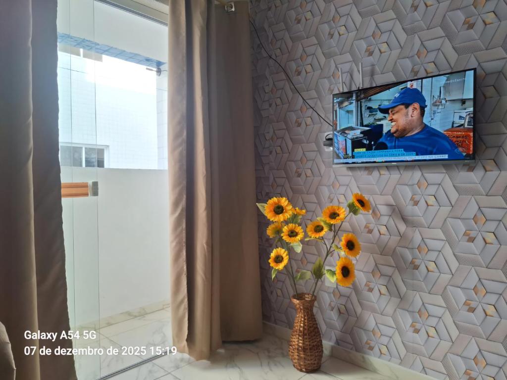 a television mounted on a wall with a vase of sunflowers at New apartment in João Pessoa in João Pessoa