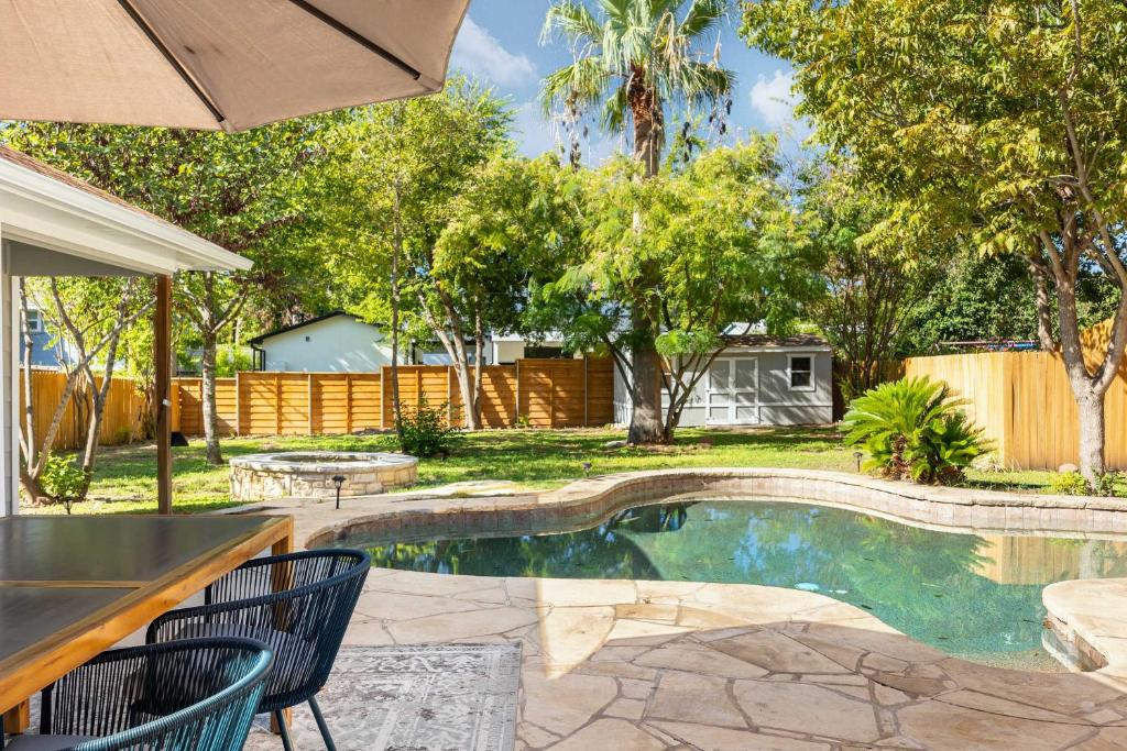 een zwembad in een tuin met 2 stoelen en een parasol bij The Oak Haven - 3BR with Pool Billiards & Arcade in Austin