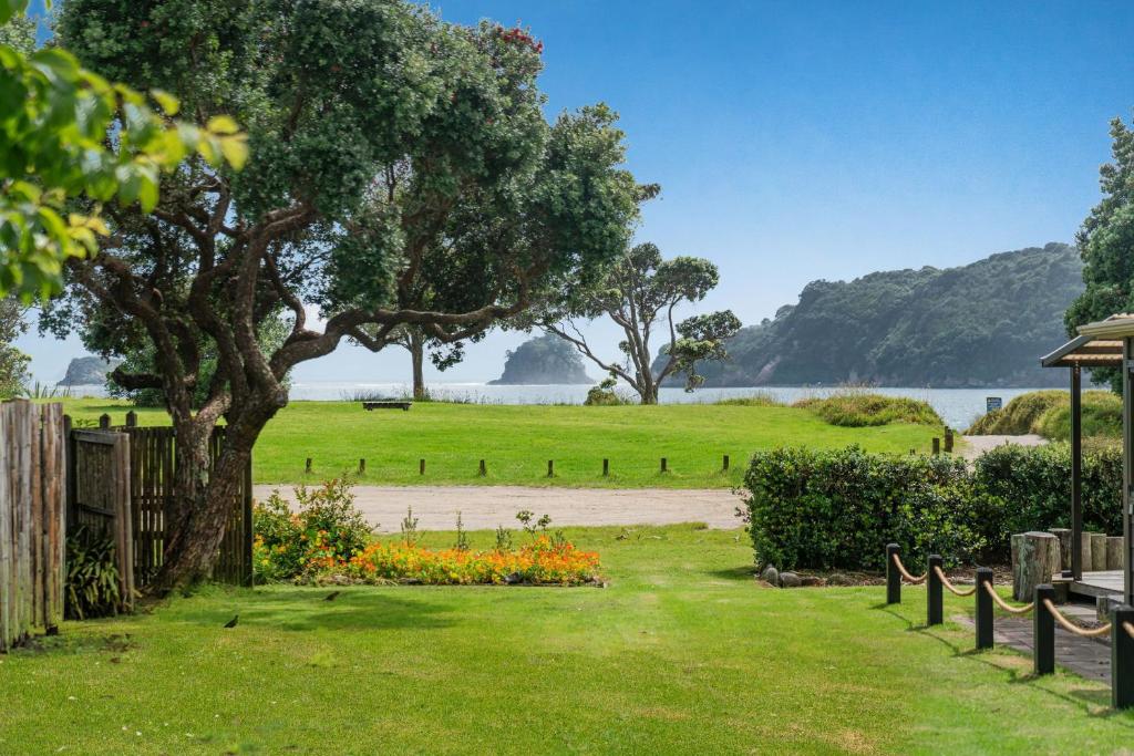a park with a tree and flowers in the grass at Hosts on the Coast Hahei Sands Villa A in Hahei