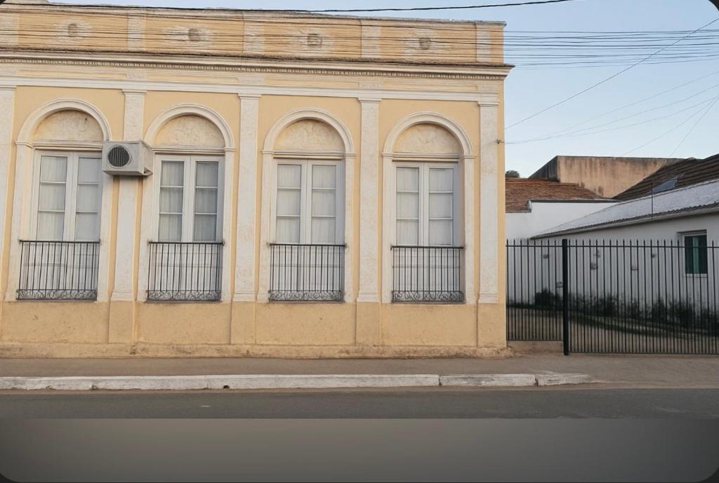 a yellow building with white windows and a fence at Casa familiar in São Gabriel