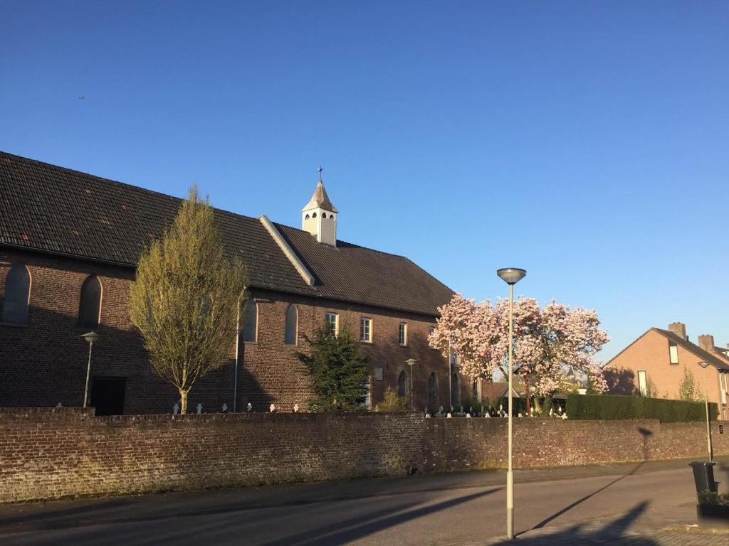 un edificio de ladrillo con una pared y árboles en la calle en B&B - Eetcafe - Riekelt en Gronsveld