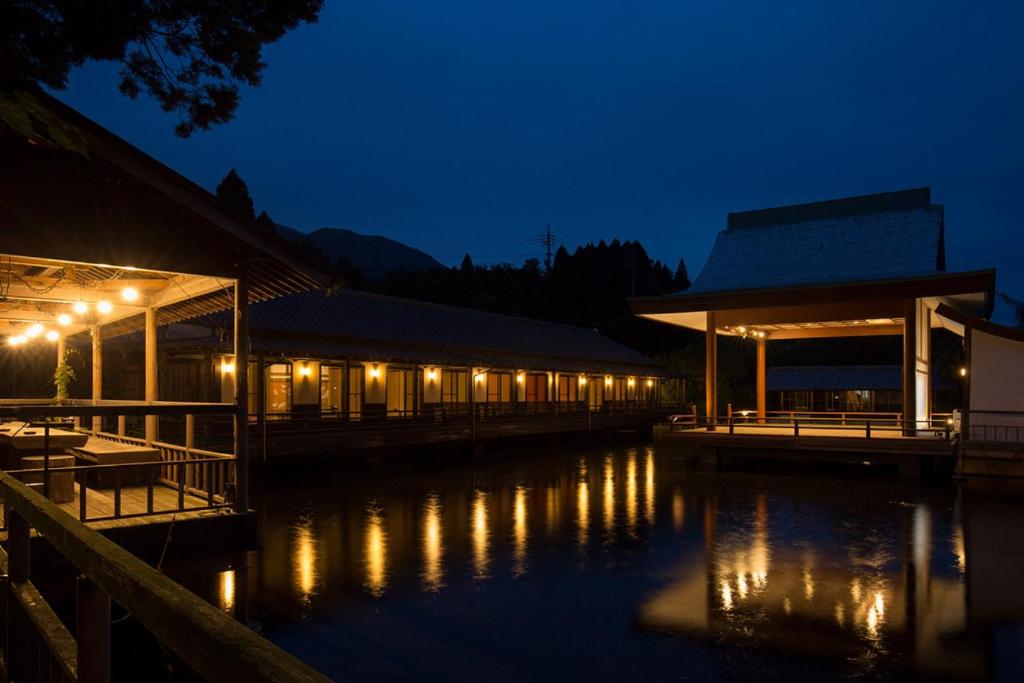 a building with lights on the water at night at Tawarayama Onsen Ryokan Minawa in Minami Aso