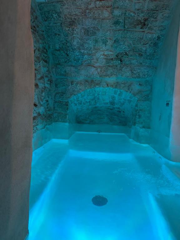 奥斯图尼Suite Le Mele的房间里有一个蓝光浴缸，旁边是一面石墙。