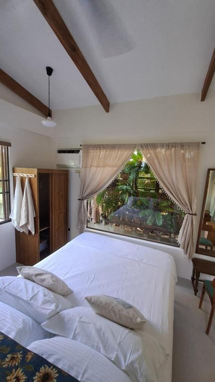 a bedroom with a large white bed with a window at Casa Munti Garden Lodge in Daet