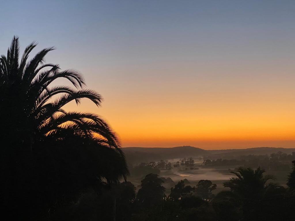 a sunset with a palm tree in the foreground at The Bloom Farm Cottage 