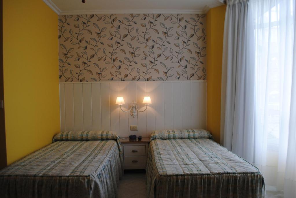 2 camas en una habitación con paredes y cortinas amarillas en Hostal Santa Marta Playa, en Baiona