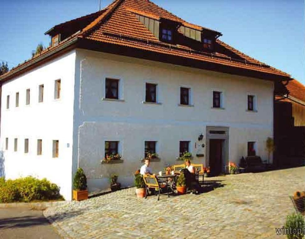 twee mensen zitten in stoelen voor een wit gebouw bij Ferienhof Aiginger in Grafenau