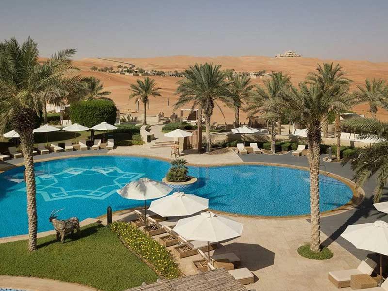 a large pool with umbrellas and palm trees in a resort at شاليهات ليوا in Al Mashrūb