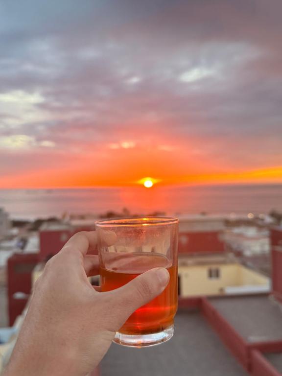 a person holding a glass of beer with the sunset in the background at Tawala House shared dorm room in Agadir