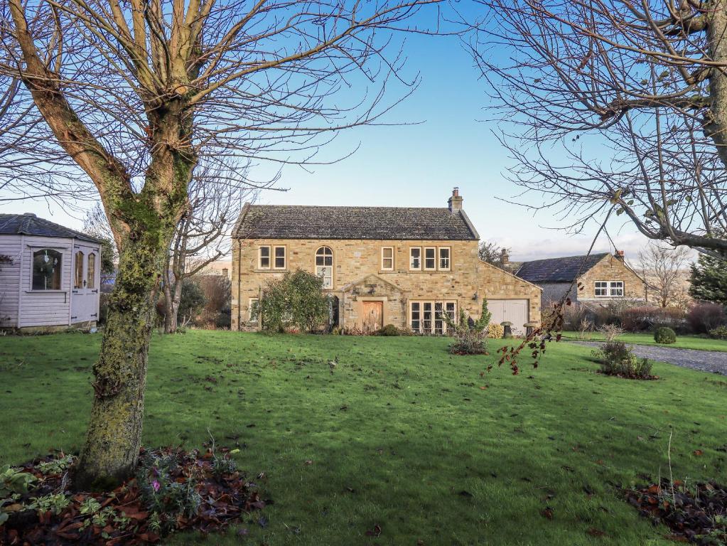 a large stone house with a tree in a field at Orchard House in Leyburn