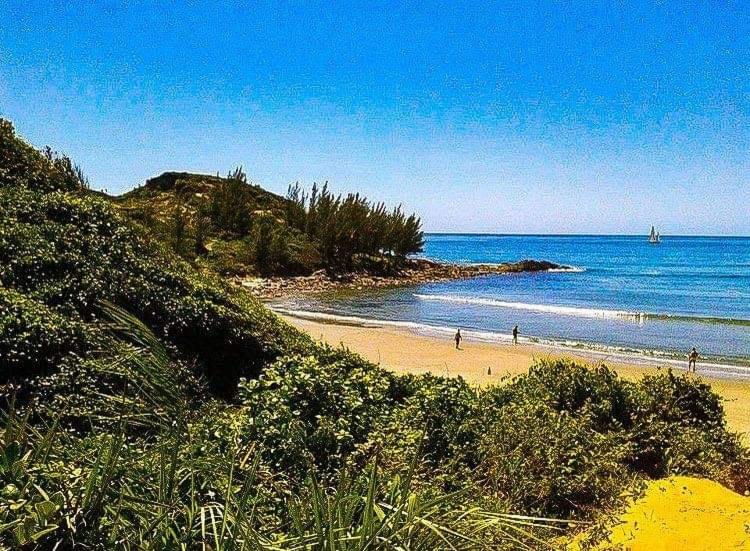 ein Strand mit Menschen im Sand und im Meer in der Unterkunft Bangalô Pé na Areia in Imbituba