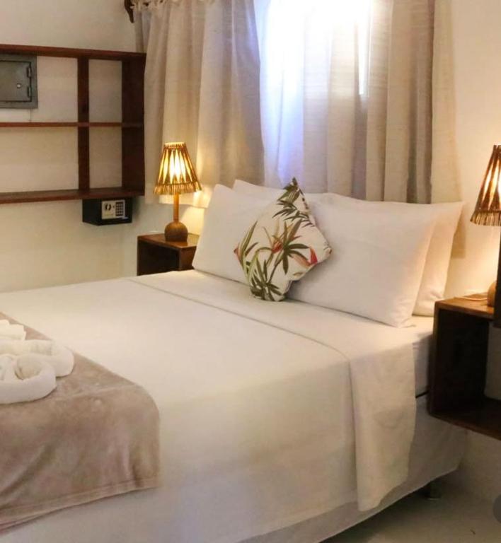 a bedroom with a white bed with two lamps at Pousada Lumawê Caraíva in Porto Seguro